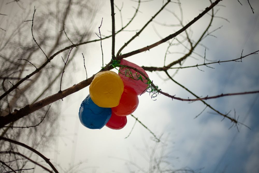 Colorful balloons caught in bare tree branches against a cloudy sky, symbolizing the tangled and unexpected consequences in navigating AI challenges.
