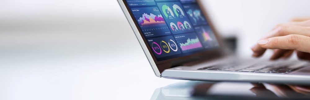 A man's hands typing on a laptop with marketing data visible on the screen.