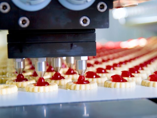 Factory automation of cookie making, lines of cookies being auto-filled with red filling from a machine.