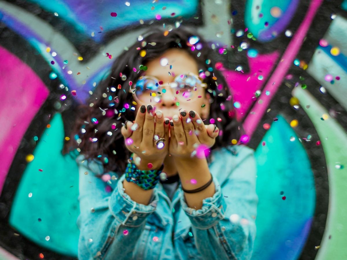 a woman blowing confetti out of her hands, towards the camera