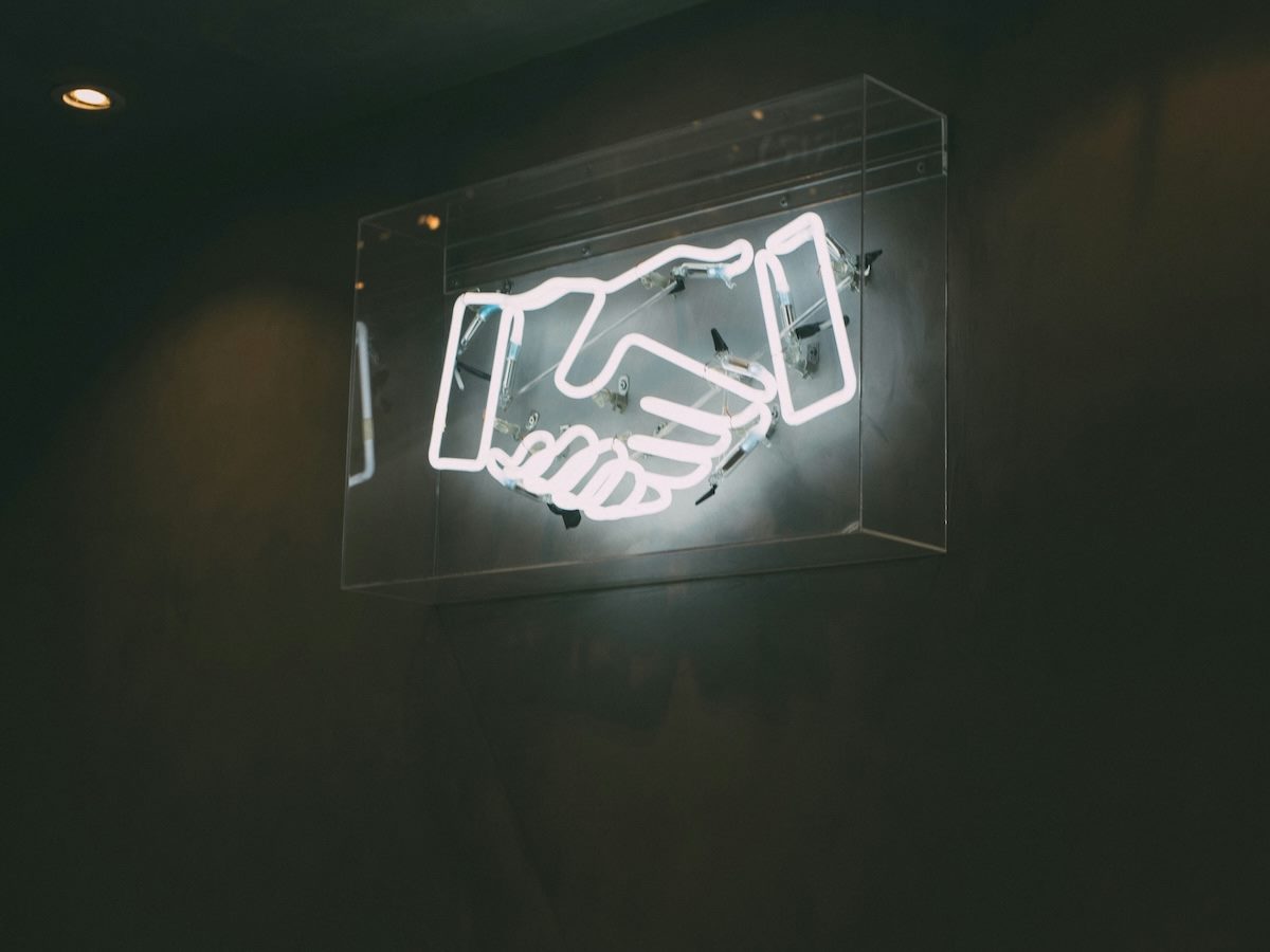 a neon sign of a handshake, suggesting partnership, collaboration