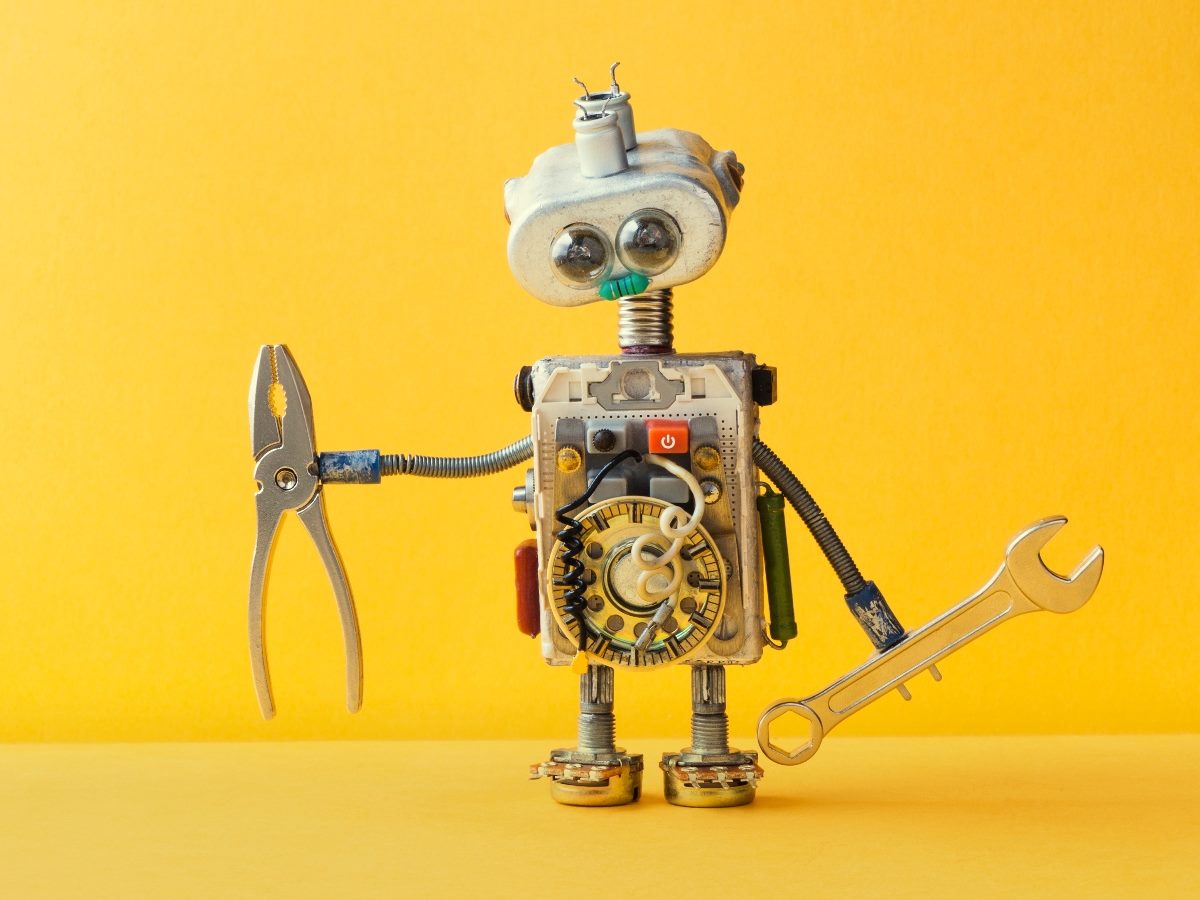 Whimsical robot made from metal parts and tools, holding pliers in one hand and a wrench in the other, standing against a bright yellow background.