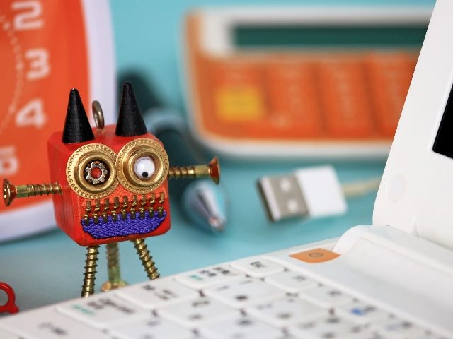Small robot figure looking over a laptop keyboard.