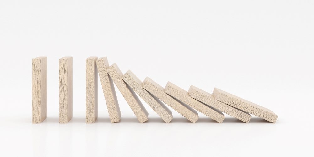 Wooden dominoes fall to one side in a piece about AI bias in CX.