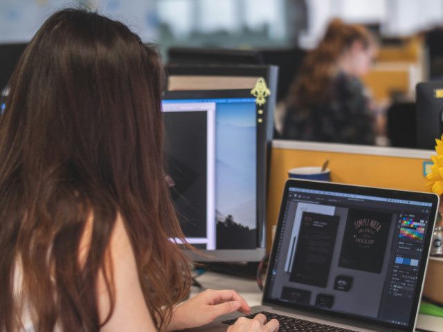 An employee works on a laptop at a desk with an external monitor.