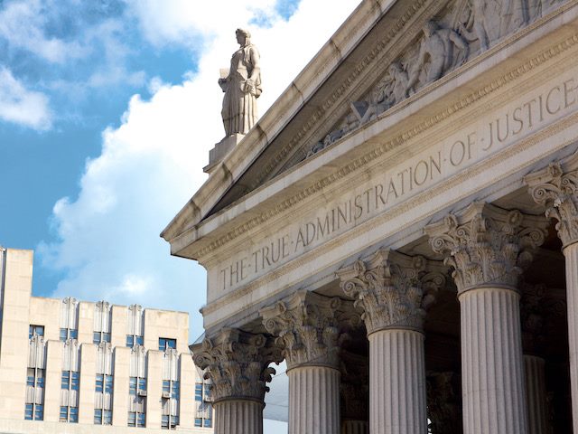 front of a New York courthouse with the text "The True Administration of Justice" inscribed across the top of the building