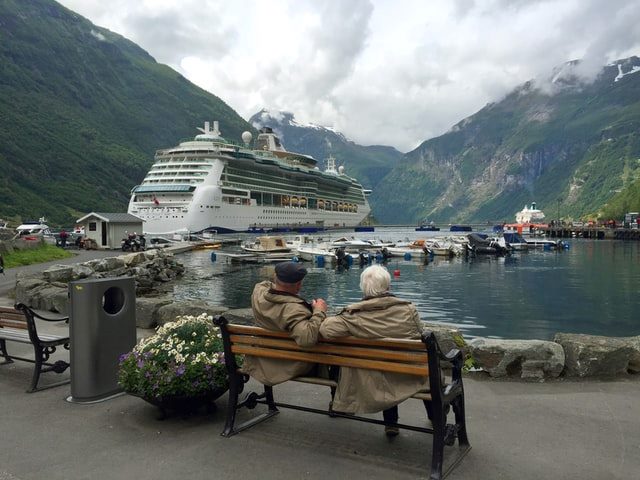 Two people sitting on a bench and looking at a cruise ship