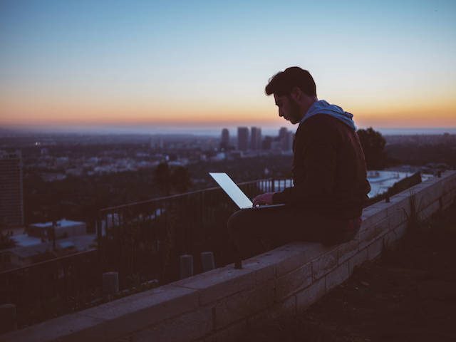 man working on laptop sitting on a parapet wall