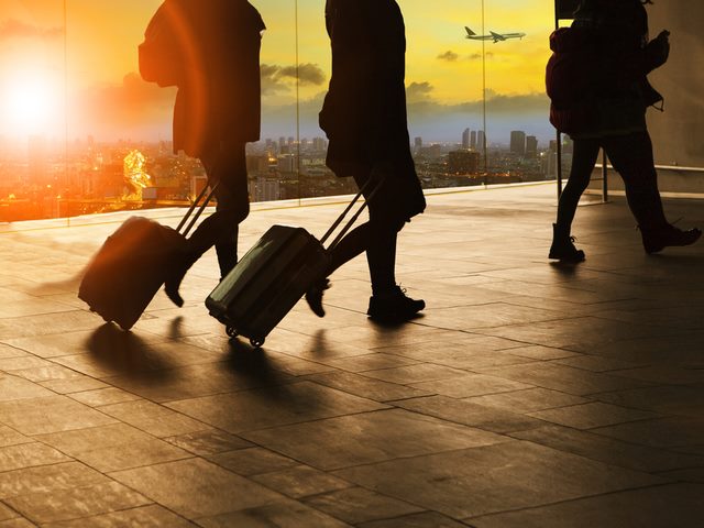 people and traveling luggage walking in airport terminal building with sun set sky at urban scene and air plane flying background