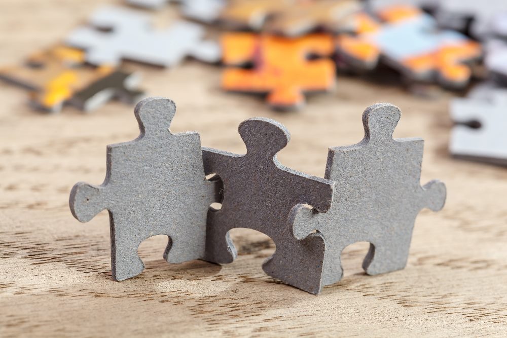 Three jigsaw puzzle pieces are linked together perched on a tabletop, suggesting the need to pursue an integrated business.