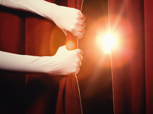 Cropped hands pulling back a red curtain to unveil a new product