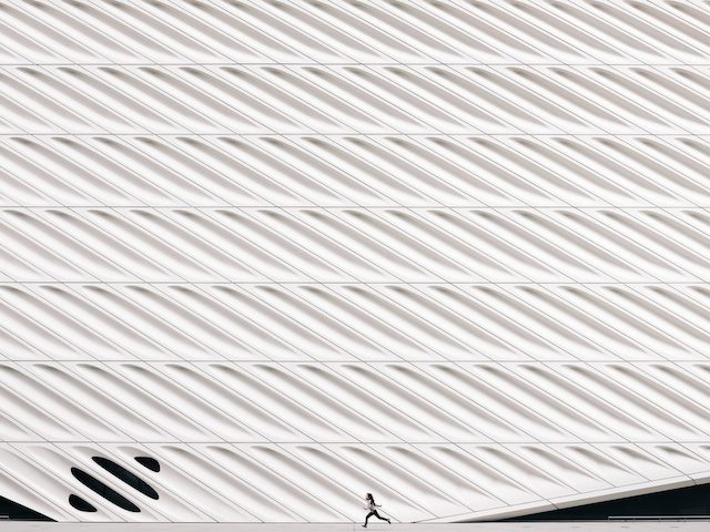 small scale person running in front of a large sculptural wall
