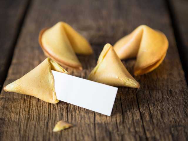A fortune cookie broken open on a wooden table. The paper inside is blank