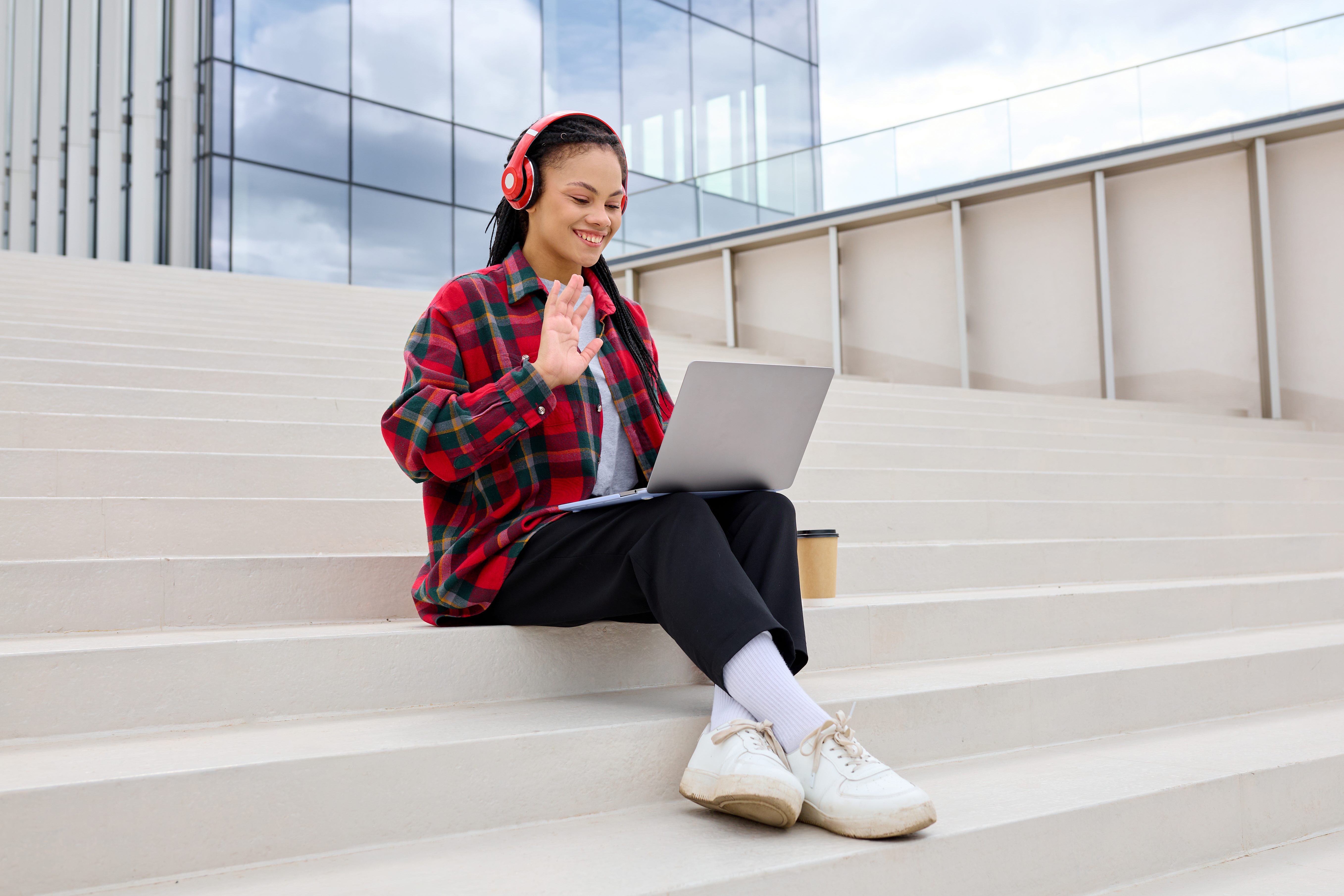 Person with headphones, sitting on steps outside on a video call on laptop