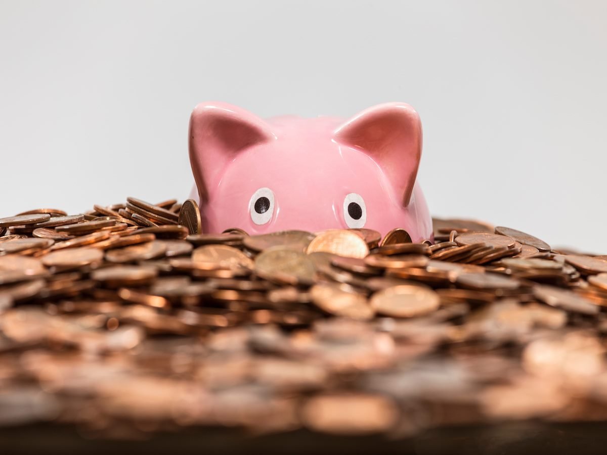 A pink piggy bank half-submerged in a pile of pennies