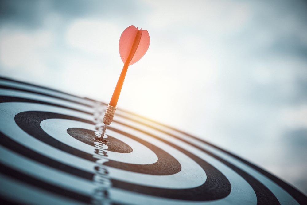 A dart has hit the target in the center of a black and white dart board with the sun and sky in the background, suggesting how AI martech is helping target customers.
