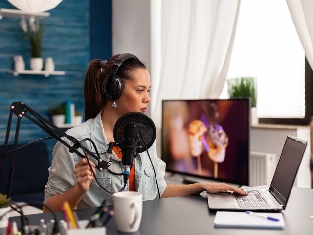 Woman wearing headphones and surrounded by digital equipment including a laptop and microphone. 