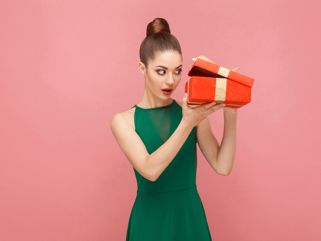 A woman unboxing a new product packaged in a red gift box. She is looking inside with anticipation of something great. AI and product discovery concept 