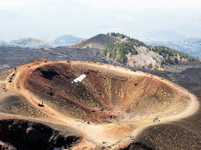 people walking  around the perimeter of a large crater  in Italy