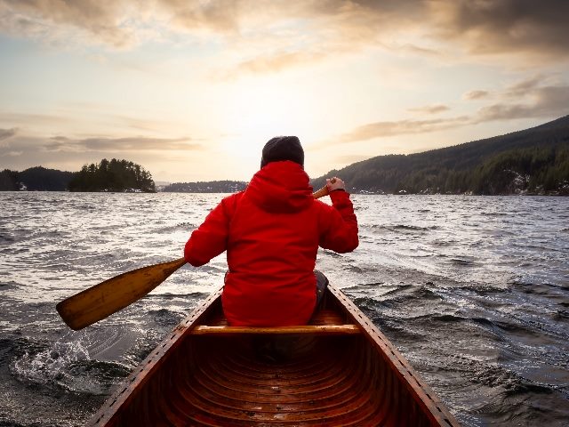 A person in a wooden canoe is paddling in the ocean with a dramatic sunset and sky, taken in Indian Arm, North of Vancouver, British Columbia, in story about AI and customer journeys. 