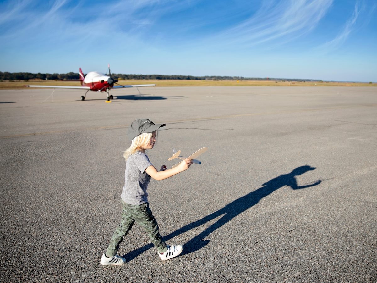 little kid playing with a toy airplane on the tarmac. small real plane in the background