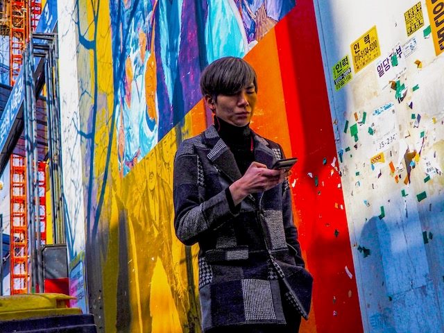 a man looking at his cellphone while walking past a colorful mural