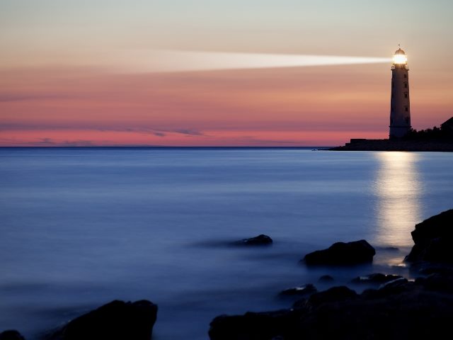 A lighthouse shines a beacon across the water at dusk on the coast with a beautiful sunset in piece about Retrieval Augmented Generation .