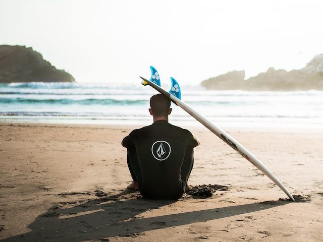Surfer sitting on the sand with the board resting on his head