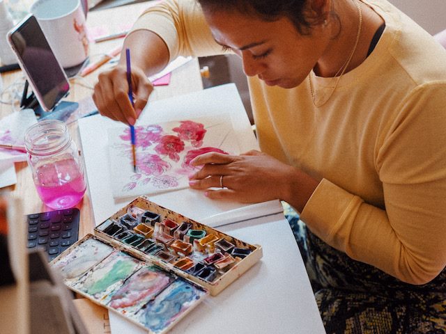 woman painting watercolor flowers at her desk