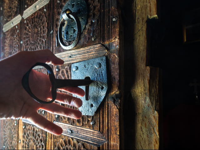 A hand unlocking rustic door of wooden church with a big key - unlocking customer data insights concept