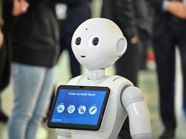 Robot interacting with customers at automation fair in Turin, Italy. It is holding a laptop with Italian words, "cosa vorresti fare," which means, "what would you like to do."