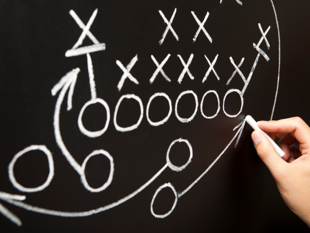 A coach drawing American football game strategy on blackboard.