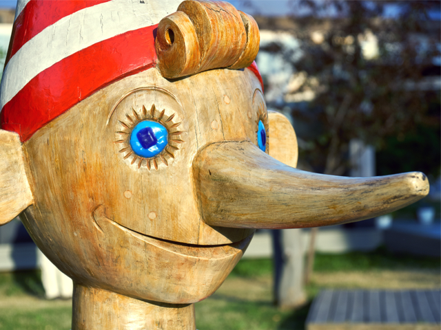 ead of wooden Pinocchio sculpture standing outdoors - lying to investors concept.