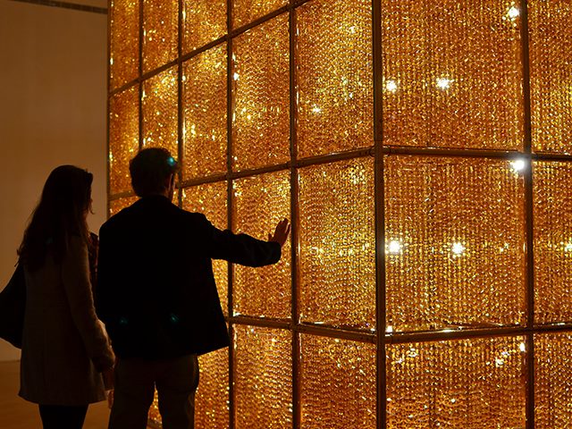 A woman and a man are looking at a large cube of crystals backlit by lightbulbs. 