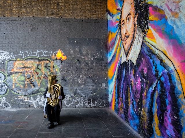 musician playing next to a Shakespeare mural in London