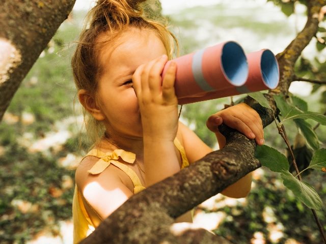 Closeup of young little girl looking through binoculars while leaning on a branch. 