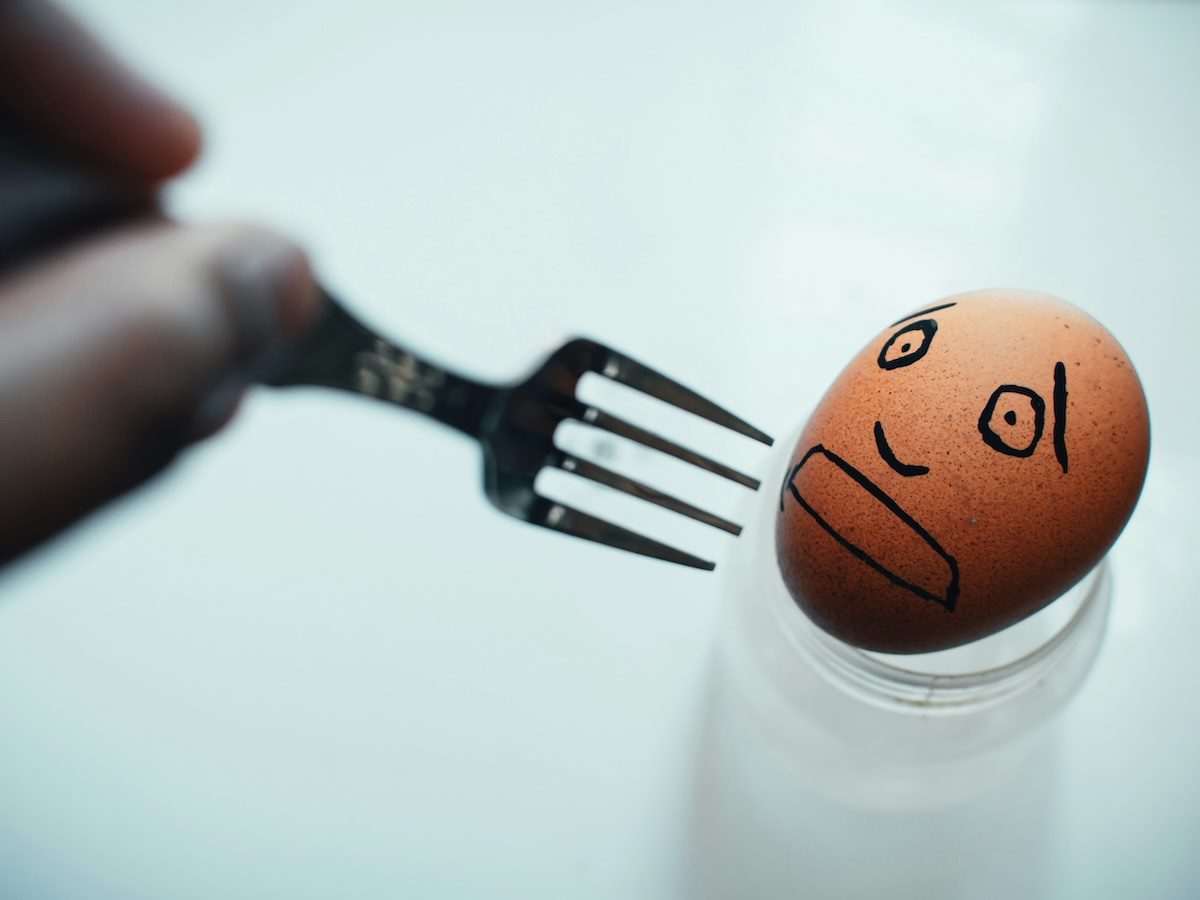 an egg with a worried face drawn on it threatened by a fork