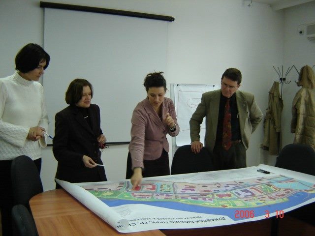Employees gather around a table observing a large chart.