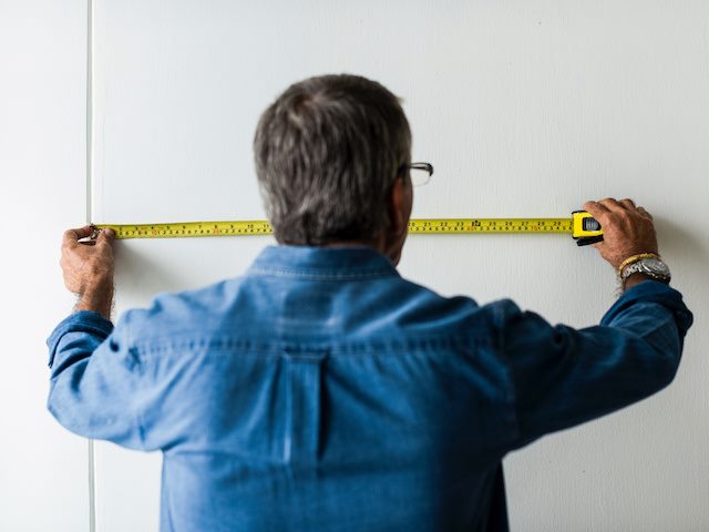 man holding measuring tape up against a wall