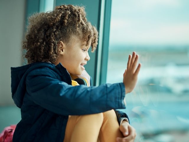 Girl child, waving goodbye out a window at an airport. 