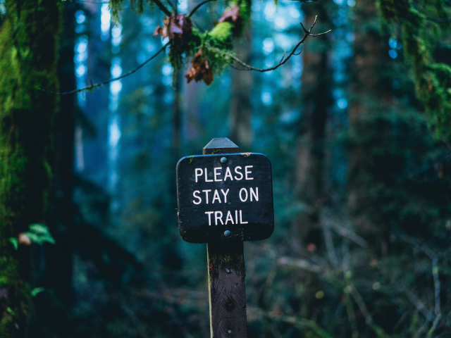 Trailhead sign in a wooded trail that reads please stay on the trail - customer retention concept