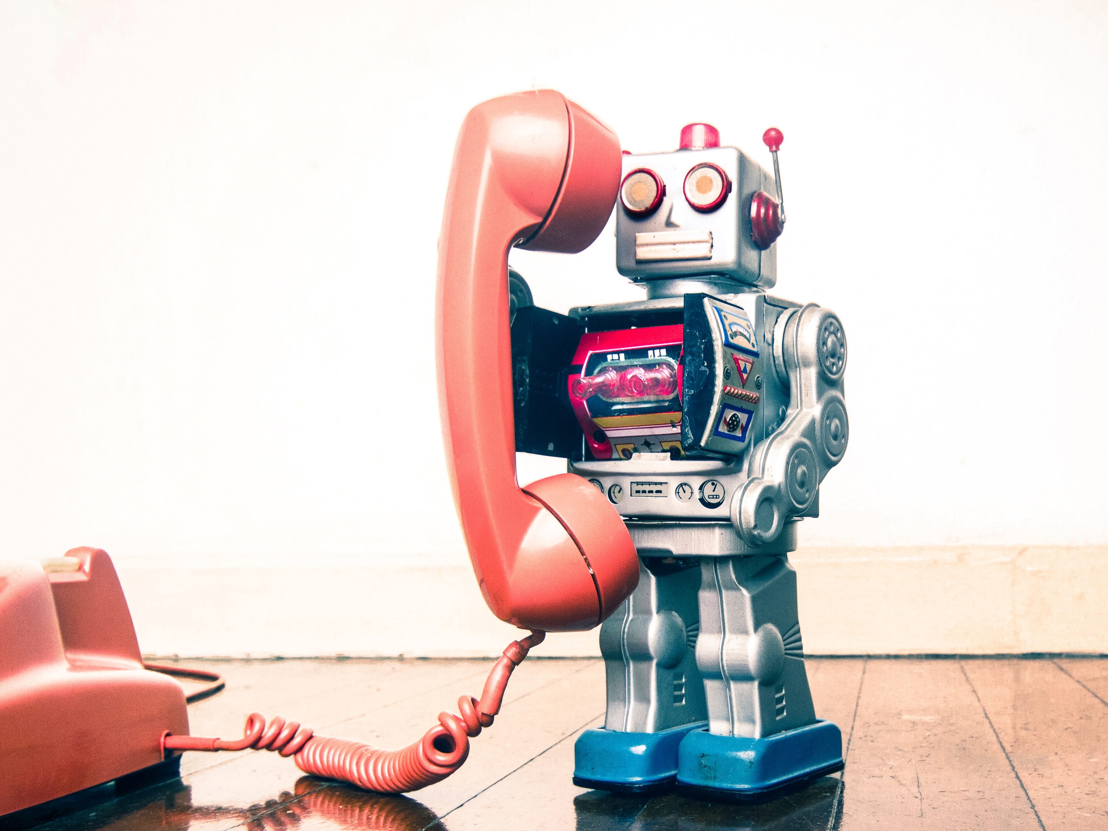 Big silver robot toy on a retro orange phone standing on an old wooden table. 