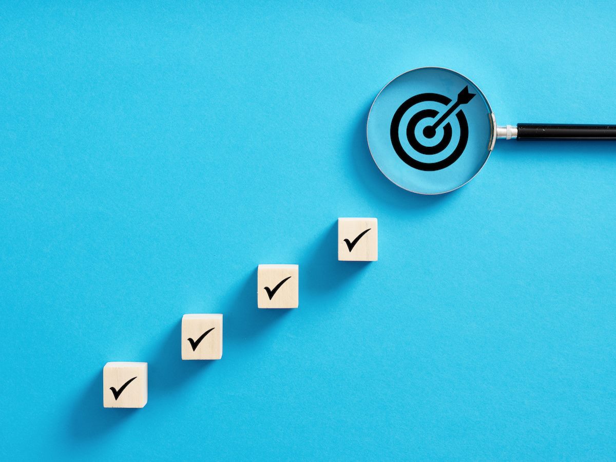 Four boxes with checkmarks inside leading up to a magnifying class with a target inside 