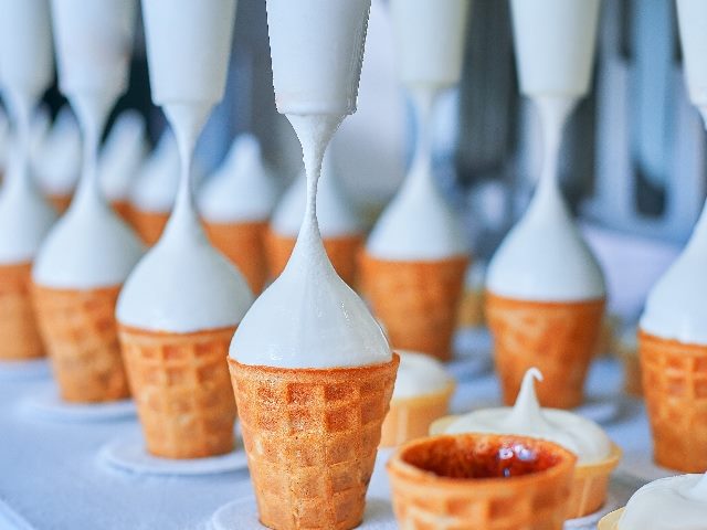 Ice-cream dairy factory:  conveyor belt with ice cream sugar cones being filled vith vanilla soft serve ice cream at modern food processing factory. suggesting the importance of marketing automation. 