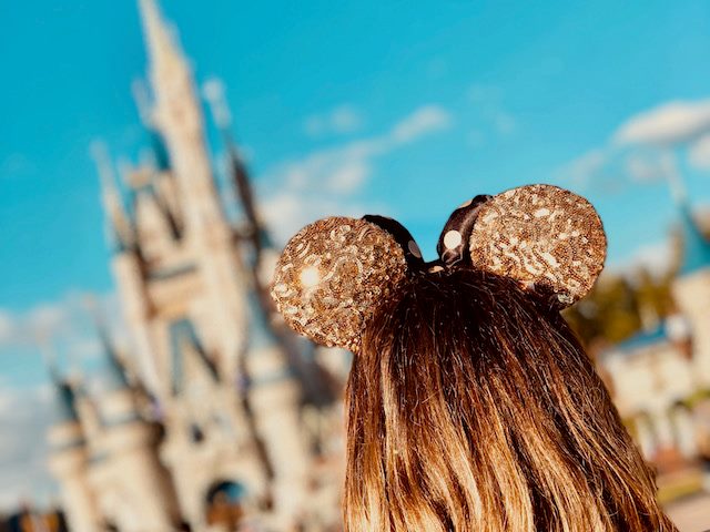 close up of the back of a little girl's head wearing mouse ears with Disney World in the background