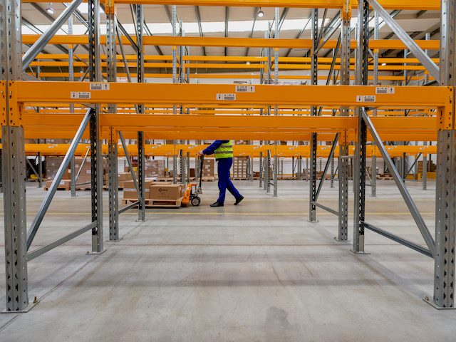 a warehouse worker whose face is hidden behind rows of metal shelving