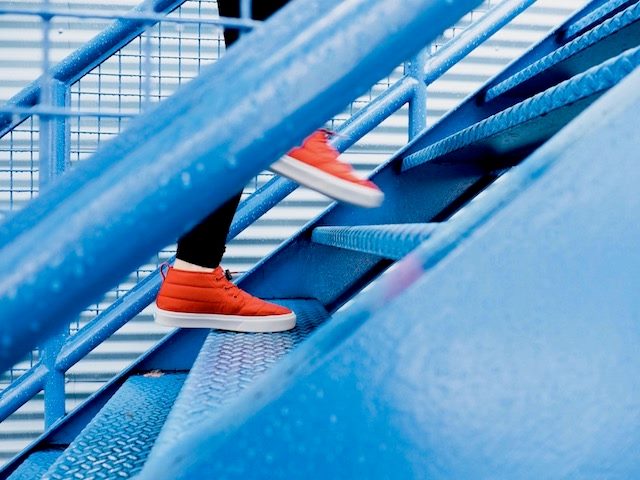 person wearing orange sneakers walking up blue stairs
