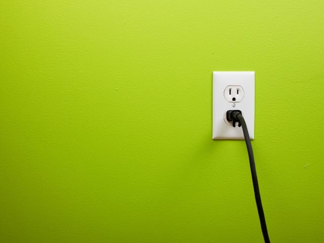 White electrical outlet on the right with a black electrical cord plugged in on lime green wall background