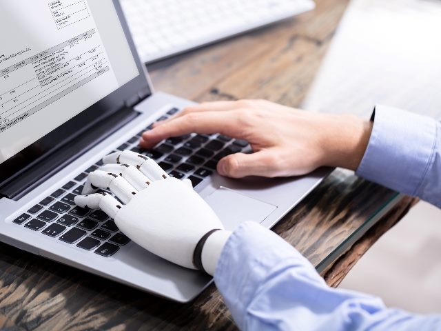 Man with prosthetic hand working on laptop, symbolizing robot/artificial intelligence doing work.