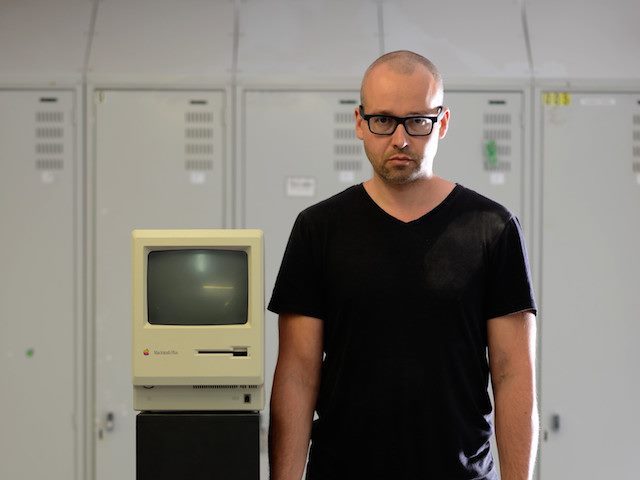 man standing next to an old Apple computer